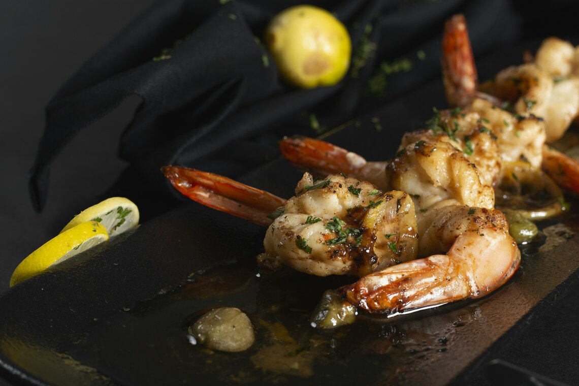 Shrimp in lemon butter with lemon wedges on a dark slate