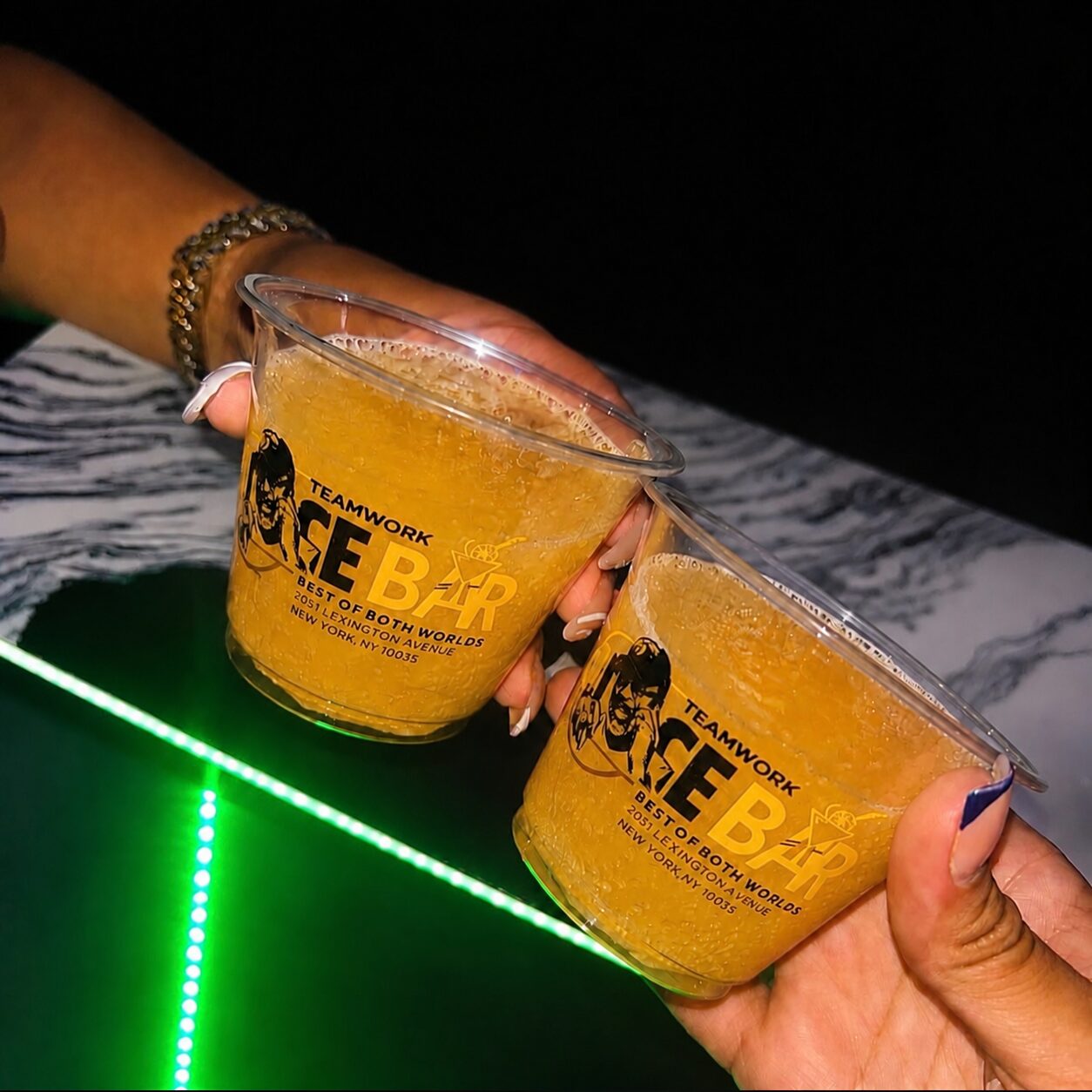 Two frozen drinks in Teamwork Ice Bar cups touching over a green-lit table